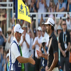 Aaron Rai and his caddie shake hands near the 18th hole flag at the PGA Championship, celebrating Aaron Rai's first major, with a cheering crowd in the background.