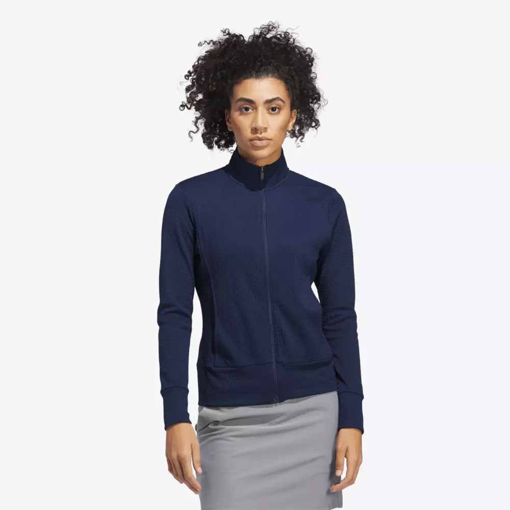 A woman with curly hair wears a blue zip-up jacket and a light gray skirt, displaying elegant attire perfect for Mother's Day, against a plain white background.