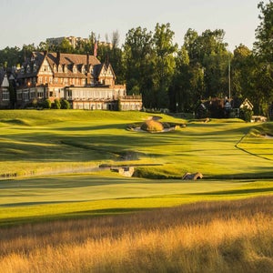 A large clubhouse with Tudor-style architecture overlooks a lush, green golf course&mdash;one of the premier PGA Championship venues&mdash;surrounded by trees and golden grasses on a sunny day.