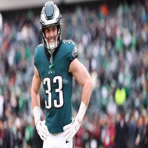 A football player wearing a green Philadelphia Eagles jersey with the number 33 stands on the field smiling, with fans blurred in the stadium background.