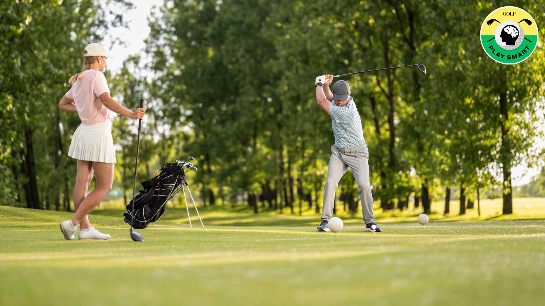 golfer swings while another golfer looks on