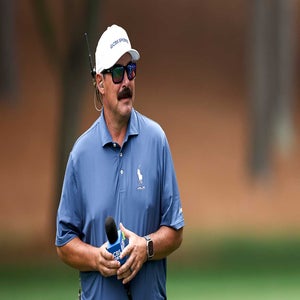 Johnson Wagner, wearing sunglasses, a headset, and a blue polo shirt, holds a CBS Sports microphone while standing outdoors on a golf course.