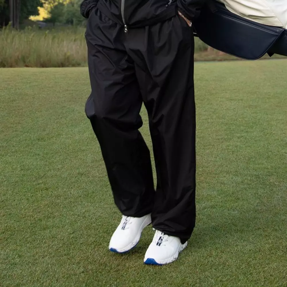 The person standing on the grass wearing black pants and a black jacket, with white athletic shoes that have blue soles—perfect for checking out the 6 golf deals worth buying right now. Their upper body is mostly out of frame.