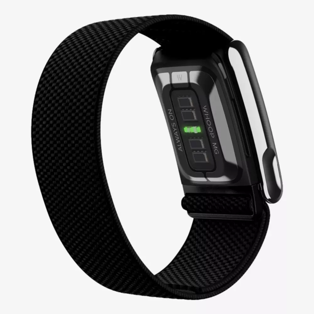 A black fitness tracker with a fabric strap is shown from the back, displaying its heart rate sensor and metallic clasp. The screen indicates text and a green light from the sensor—proof that summer is the right time to stay active, rain or shine!.