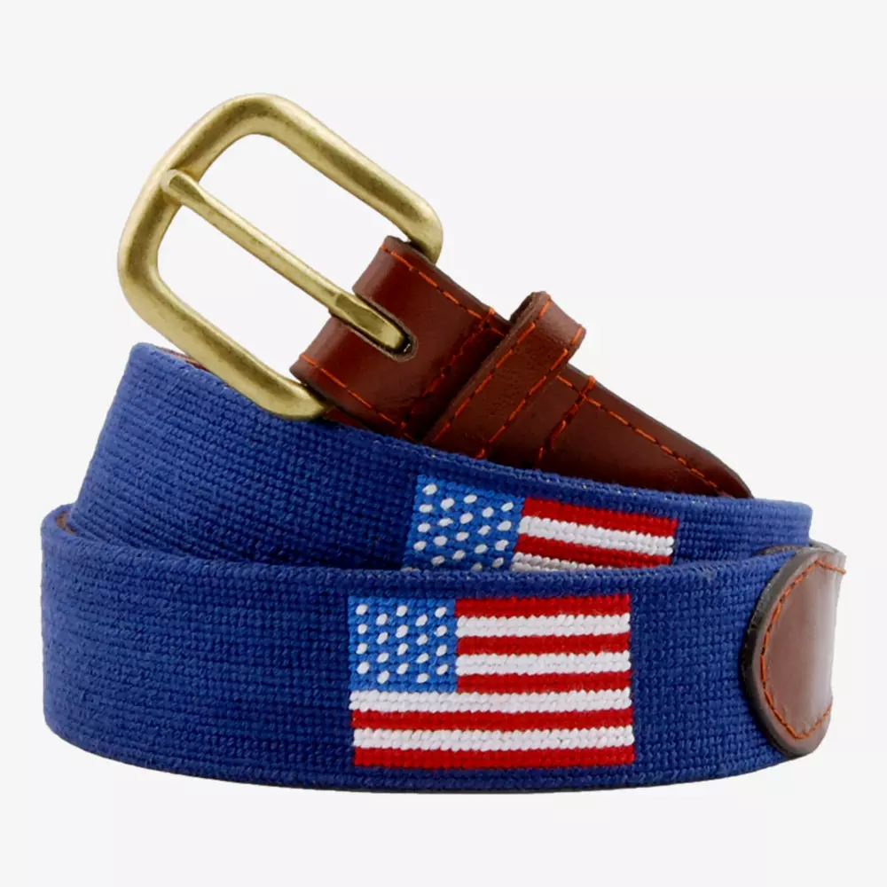A blue fabric belt with brown leather accents and a brass buckle, featuring embroidered American flags—perfect for those seeking the best golf deals for around $250.