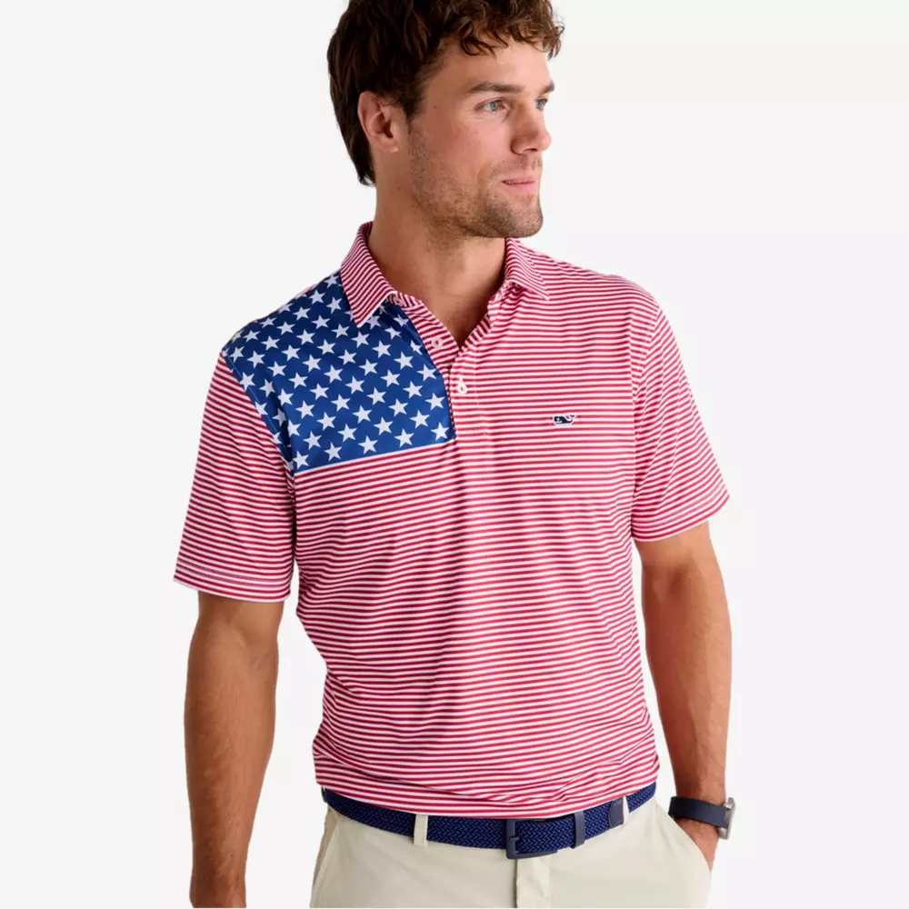 A man wearing a red and white striped polo shirt with a blue section covered in white stars on one shoulder, tan pants, and a navy belt—styled perfectly for those seeking the best golf deals for around $250—looks to the side against a plain background.