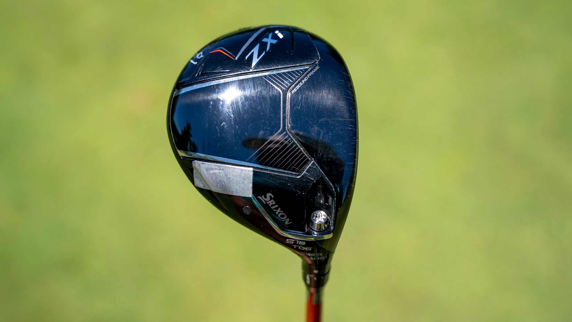 A close-up of a Srixon ZX golf club driver with a black, shiny head and silver details sits against a blurred green background, reminiscent of the style seen in Tour Report features on drivers like the Titleist GTS driver.