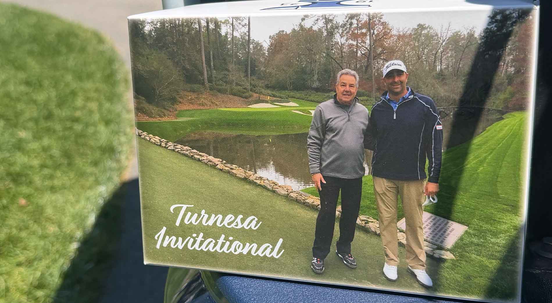 Two men stand side by side on a golf course near a pond, smiling at the camera. A Sony camcorder captures the moment. The text Turnesa Invitational is written in white script on the bottom left corner of the image.