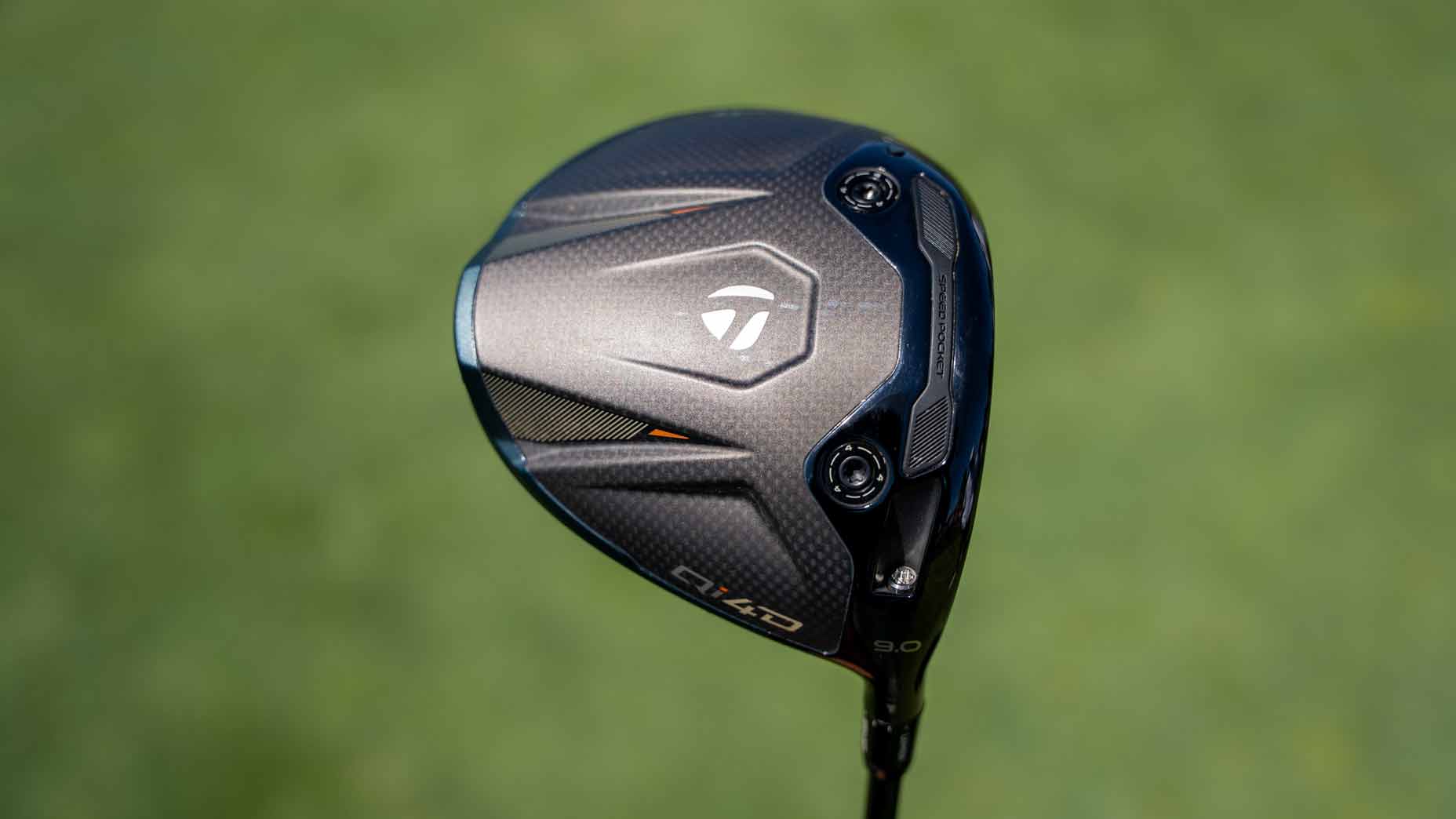 Close-up of a TaylorMade golf driver clubhead with a black and silver design, featuring logos and adjustment screws, set against a blurred green background—a setup reminiscent of equipment found in Tour Report features or used by professionals like Tommy Fleetwood.