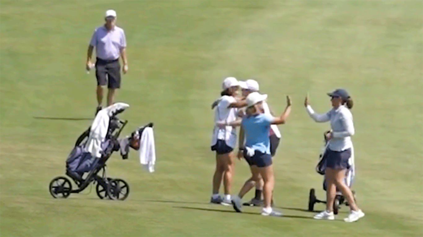 A group of female golfers celebrate on a golf course, giving high fives and hugs near a golf cart, while another person stands in the background.