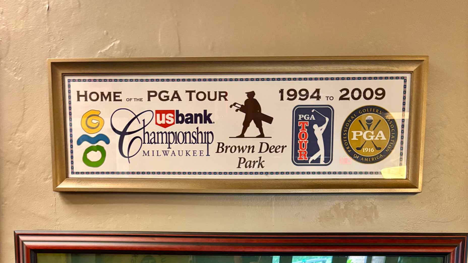 Framed sign reading Home of the PGA Tour 1994 to 2009 with logos for US Bank Championship Milwaukee, Brown Deer Park, PGA Tour, and PGA of America on a beige wall—an ideal inspiration piece for anyone planning an affordable golf vacation or memorable Wisconsin golf trip.